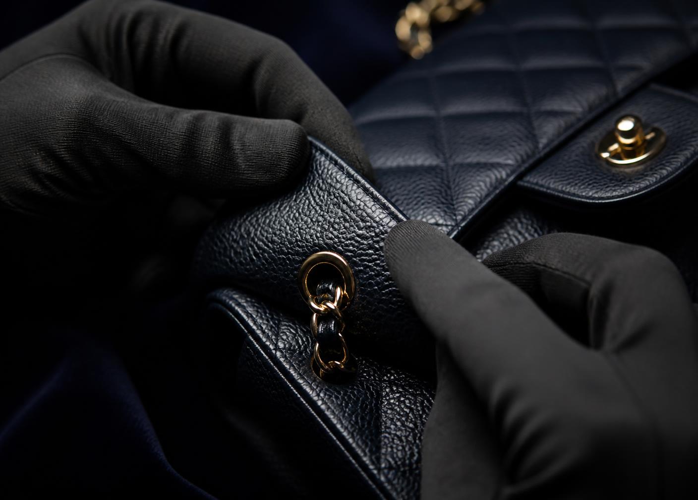 A quilted black leather handbag examined with black gloves during a detailed inspection