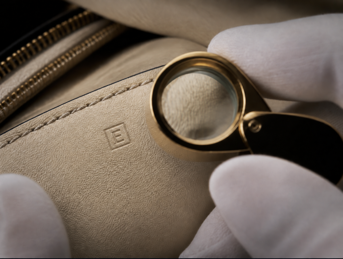 Close-up of cream leather, stitching and a magnifying loupe during a detailed luxury-fashion examination.